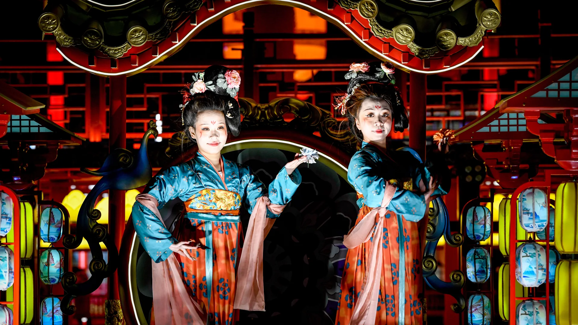 Two dancers in Tang-style court robes and floral headdresses performing on a lantern-lit, palace-style stage