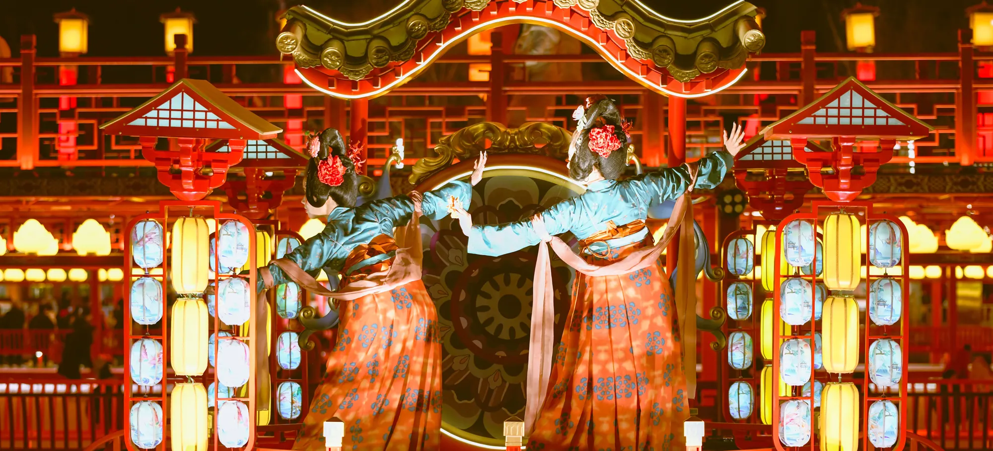 Two dancers in Tang-style court robes performing between rows of glowing lanterns on a palace-style stage